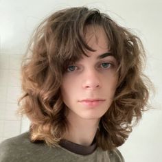 a close up of a person wearing a green shirt and long curly hair with blue eyes