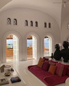 a living room filled with white furniture and lots of arched windows overlooking the ocean in front of it