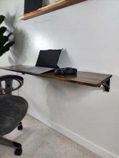 a laptop computer sitting on top of a wooden shelf next to a black office chair