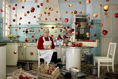 an older woman sitting in a kitchen with apples falling from the ceiling and on the counter