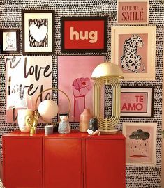 a red cabinet sitting in front of a wall with pictures and art on the walls