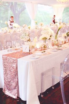 the table is set with clear chairs and white flowers in vases on each side