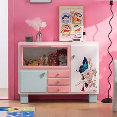 a pink and white cabinet with pictures on the wall next to a chair in a living room