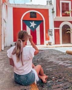 a woman sitting on the ground in front of a red and white building