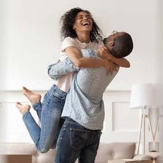 a man holding a woman in his arms while they are standing on the floor and laughing