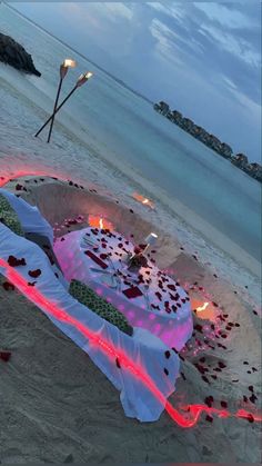 a table is set up on the beach with candles and petals laid out in the sand