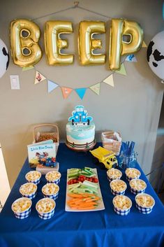 a blue table topped with lots of food next to balloons and buntings on top of it