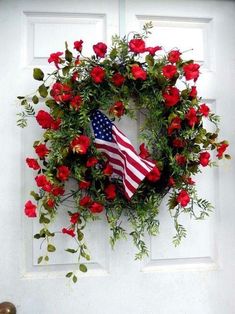 a wreath with an american flag and red flowers on it hanging from the side of a door