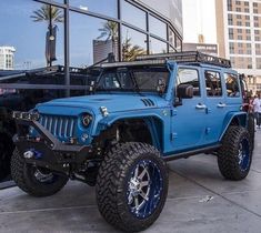 a blue jeep is parked in front of a building with people standing around it and looking at the windows