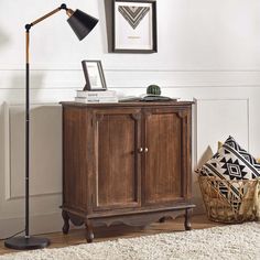 a wooden cabinet with a lamp and pictures on the wall above it in a living room