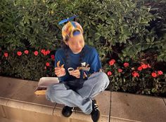 a young boy sitting on top of a cement wall next to plants and flowers wearing a graduation cap