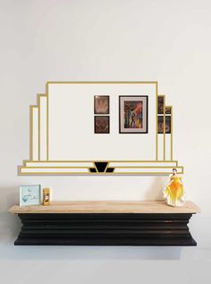 a white and gold wall mounted mirror on top of a wooden shelf next to a vase with flowers