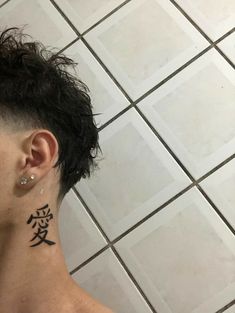 a person with a tattoo on their neck and behind his ear, standing in front of a tiled floor