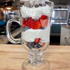 a glass mug filled with fruit and whipped cream on top of a wooden countertop