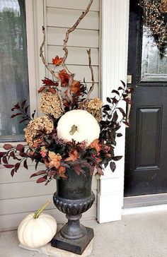 a black vase filled with white pumpkins sitting on top of a stone slab next to a door