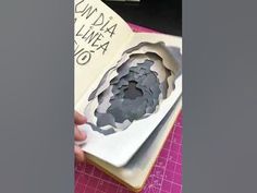 someone is holding an open book with paper cut out of it