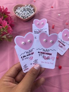 three small pink hearts are held up in front of a bowl of flowers and beads