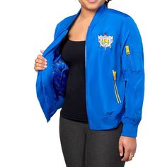 a woman wearing a blue jacket with patches on her chest and black top, standing in front of a white background