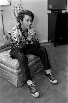 a man sitting on top of a couch next to a white dresser and holding a cup