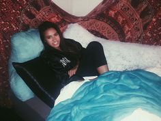 a woman laying on top of a bed next to a blue comforter and pillows