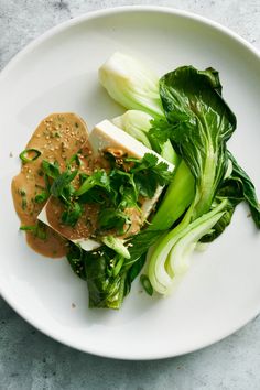 a white plate topped with green vegetables and meat covered in gravy on top of a table