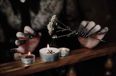 two hands holding candles with flowers in them on a wooden table next to another person