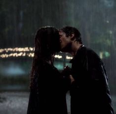 a man and woman kissing in the rain with lights shining on their faces behind them