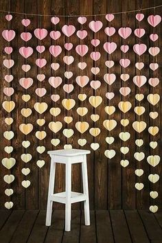 a white stool sitting in front of a wooden wall with paper hearts hanging from it