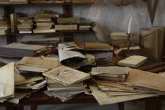 many old books are piled on top of each other in a room full of shelves