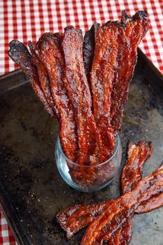 bacon sticks in a glass jar on a tray next to a checkered tablecloth