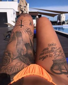 two people with tattoos on their legs sitting next to each other in front of a swimming pool