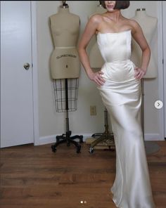 a woman standing in front of a mannequin wearing a white dress with her hands on her hips