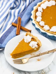 a slice of pumpkin pie on a plate with a fork and cinnamon sticks next to it