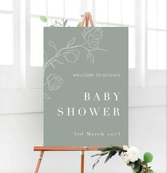 a baby shower sign sitting on top of a easel next to a flower arrangement