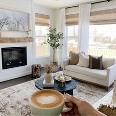 a person holding a cup of coffee in front of a fire place and couches