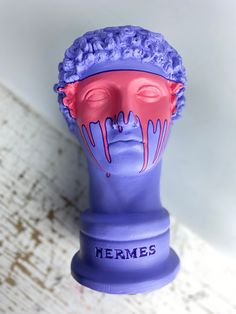 a purple mannequin head with pink paint dripping down it's face and the words mermes on its forehead