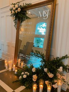 candles are lit in front of a large mirror with greenery and flowers on it