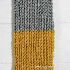 a knitted yellow and gray blanket sitting on top of a wooden floor next to a white wall