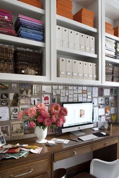 a desk with a computer and flowers on it in front of some bookshelves