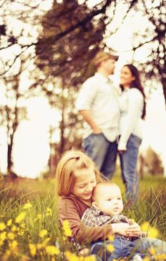 a couple and their child are sitting in the grass with yellow flowers around them on a sunny day