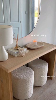 a table with two stools and a round mirror on the wall above it, next to a lamp