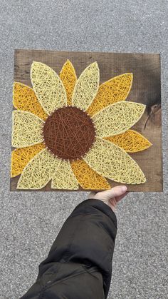 a person holding up a piece of string art with a sunflower on it's side