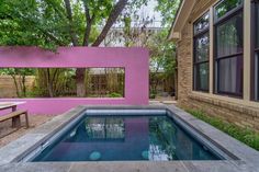 a swimming pool in front of a house with pink paint on the walls and windows