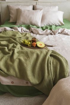 an unmade bed with green blankets and fruit on it