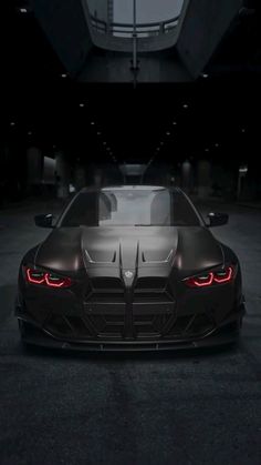 the front end of a black sports car in a dark garage with its lights on