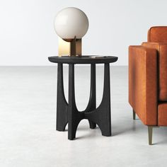 an orange chair and black table with a white ball on it in front of a brown couch