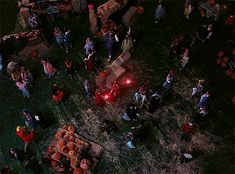 an aerial view of people standing around in the grass with red lights on their cars