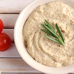 a white bowl filled with hummus next to tomatoes