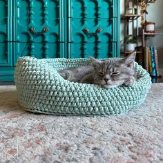 a cat is sleeping in a crocheted bed on the floor next to a dresser