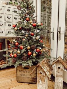 a small christmas tree in a wooden box on the floor next to a birdhouse